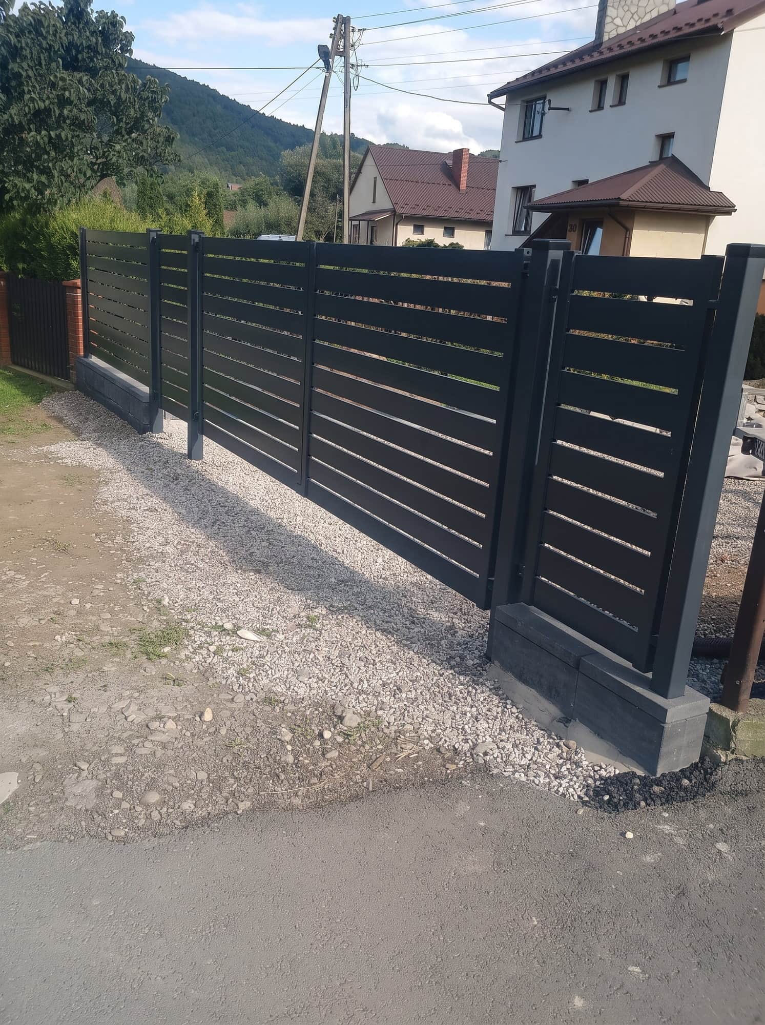 Czarna brama przesuwna z poziomych lameli na wjeździe do posesji